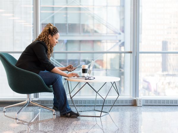 Femme assise se penchant vers son téléphone et ordinateur sur une table basse