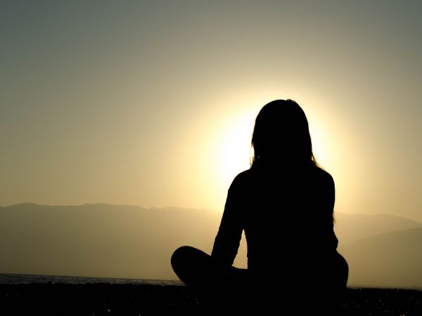 Photo d'une femme méditant face au coucher du soleil