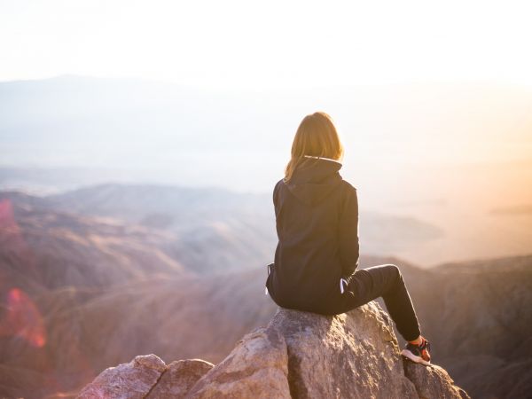 Femme regardant un paysage assise en haut d'une montagne