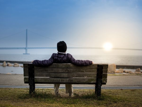 Homme assis sur un banc contemplant un coucher de soleil derrière un pont suspendu