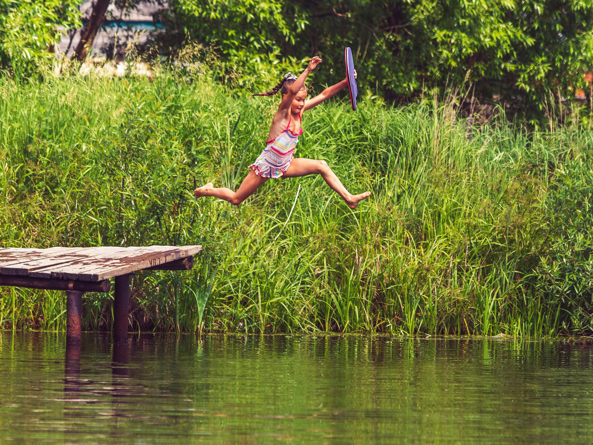 Une fille se jette dans l'eau d'un ponton en bois tenant une bouée dans la main