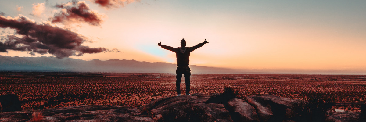 Photo d'un homme écartant les bras face à un coucher de soleil