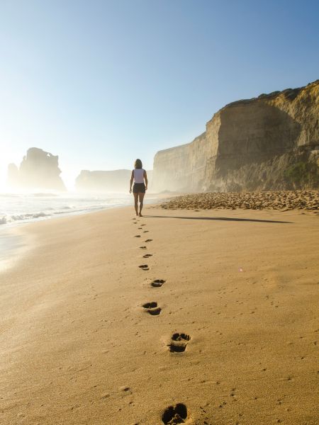 Femme marchant sur du sable laissant derrière elle des traces de pas