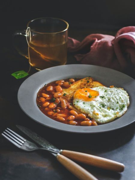 Photo d'un petit déjeuner anglais, à base d'oeuf au plat, de haricots rouges et d'un toast, accompagné d'un thé